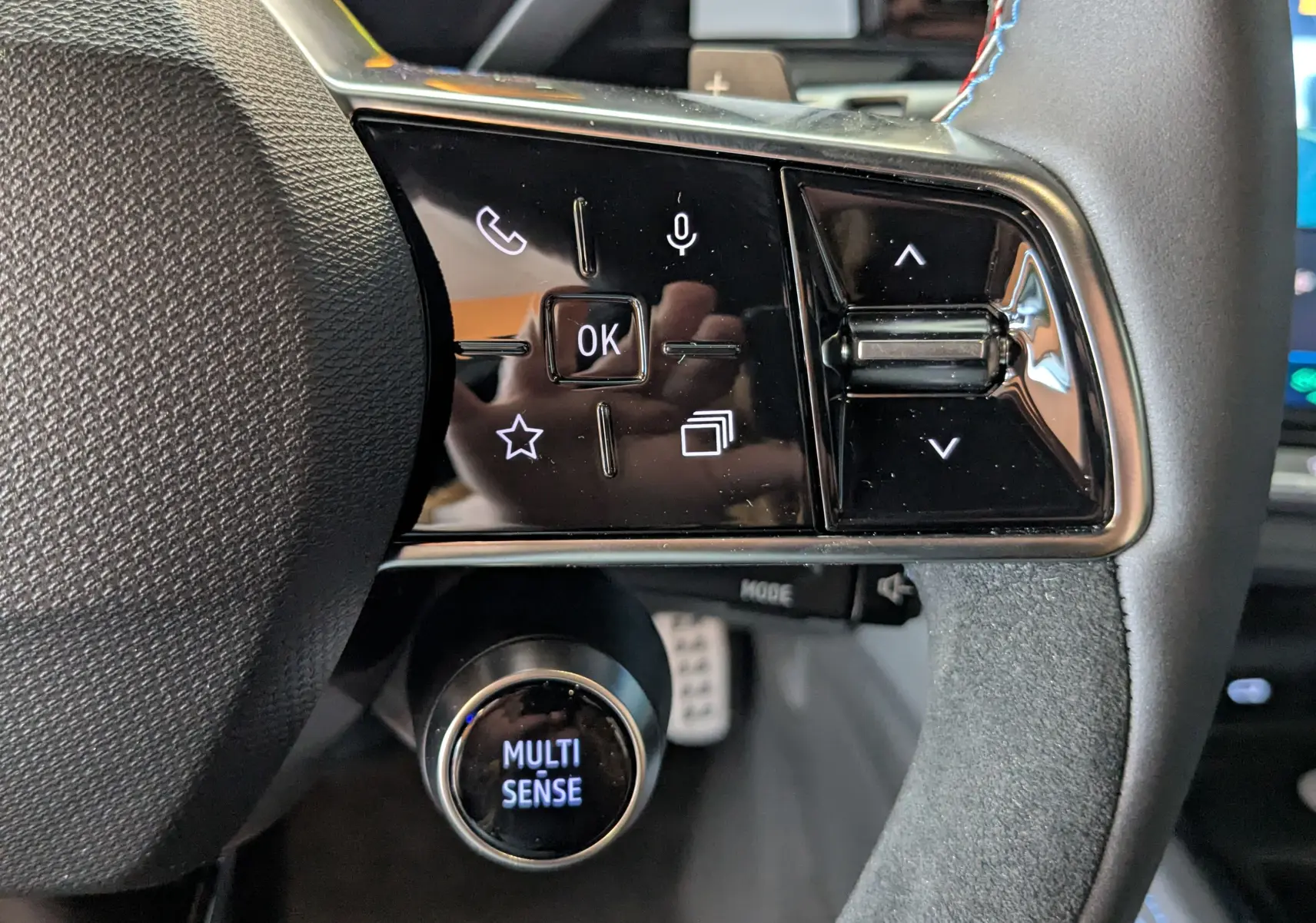 Gros plan sur les commandes au volant droit du Renault Austral gris schist, avec bouton rotatif Multi Sense éclairé.
