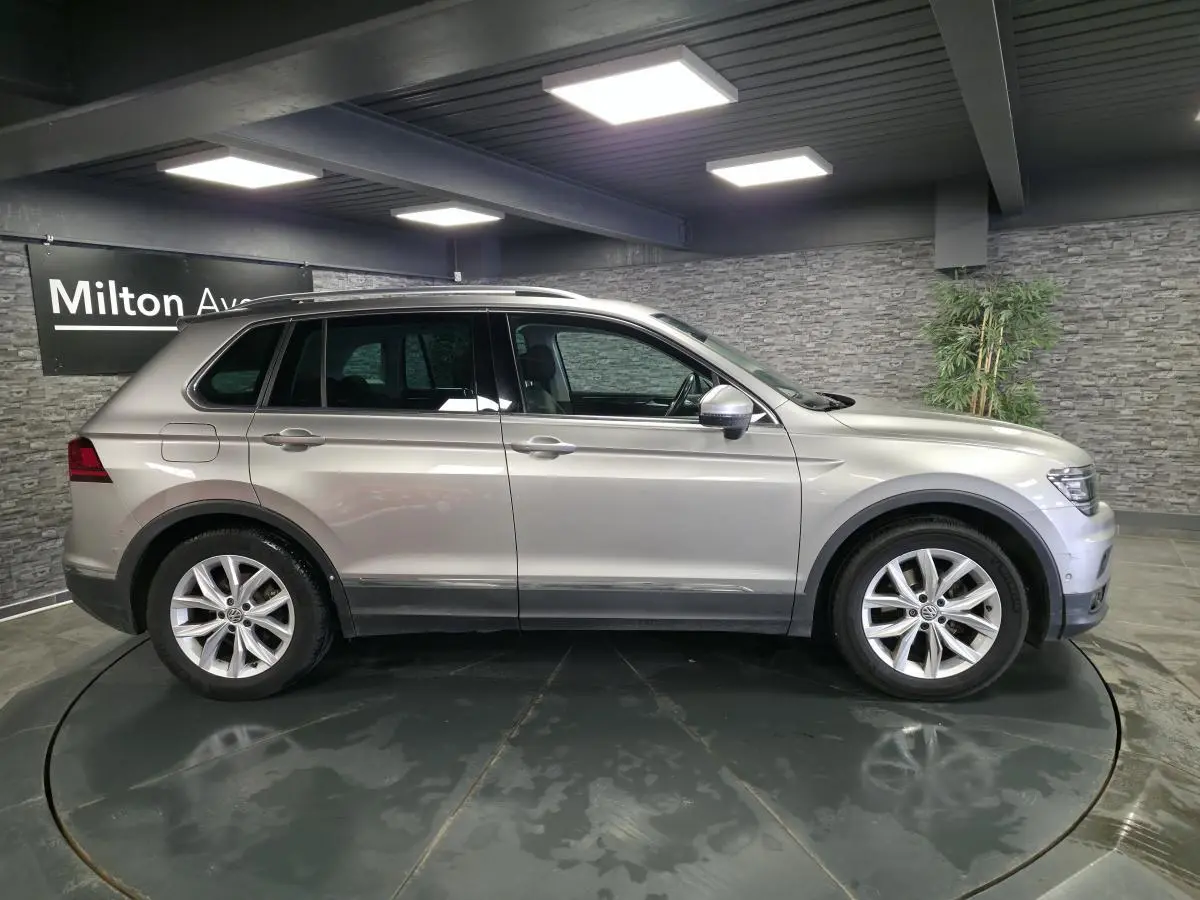 Profil droit d'un Volkswagen Tiguan gris métallisé 2020 avec jantes alliage 18 pouces dans un showroom intérieur.