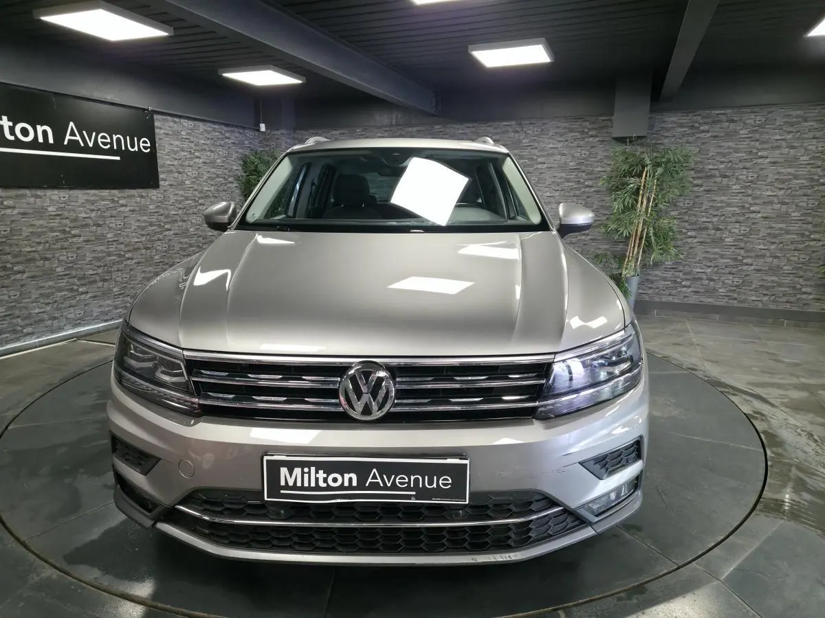 Vue frontale d'un Volkswagen Tiguan gris métallisé 2020 avec calandre chromée et phares LED allumés en showroom.
