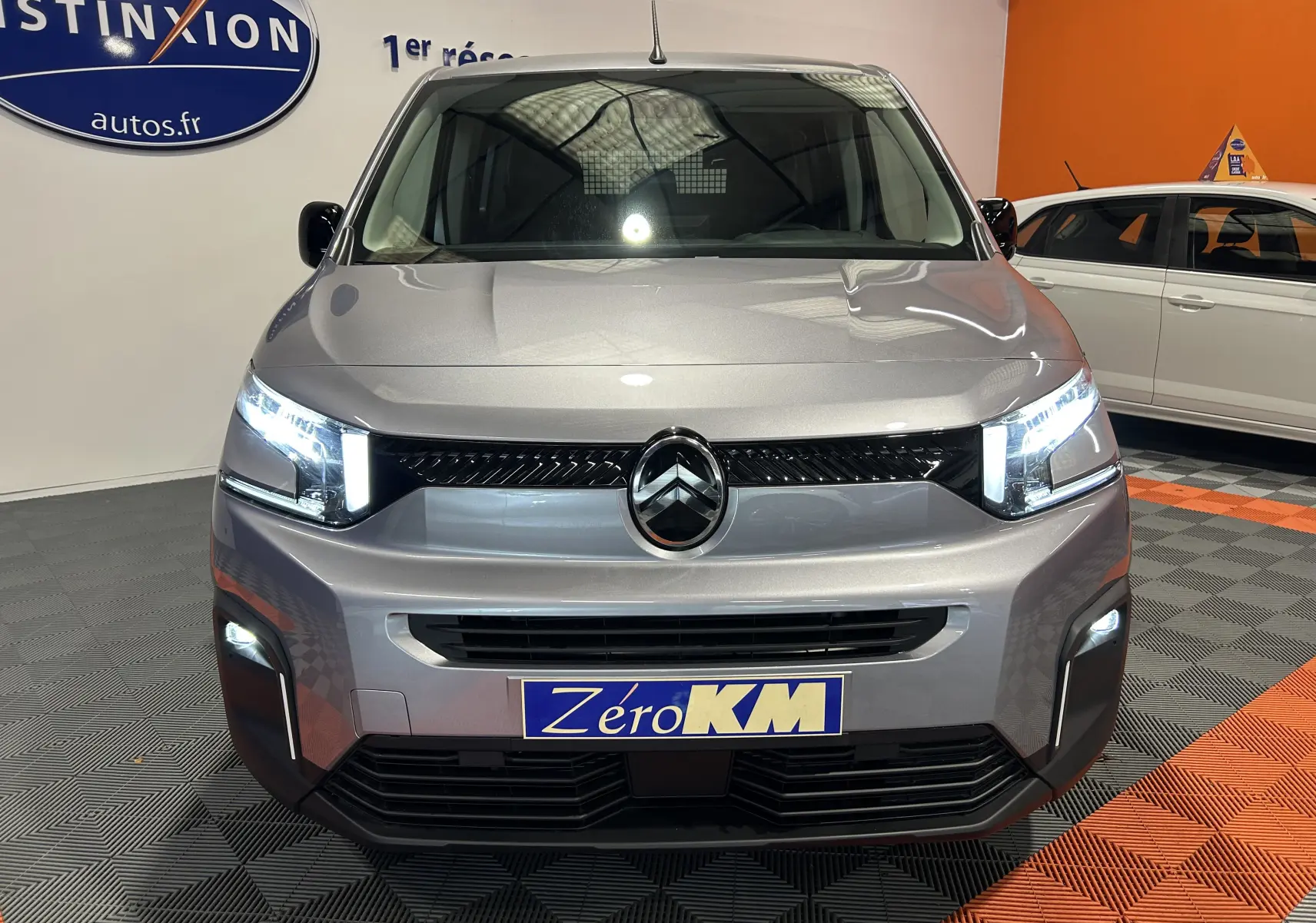 Vue avant d'un Citroën Berlingo Multispace gris Artense avec phares allumés dans un showroom.