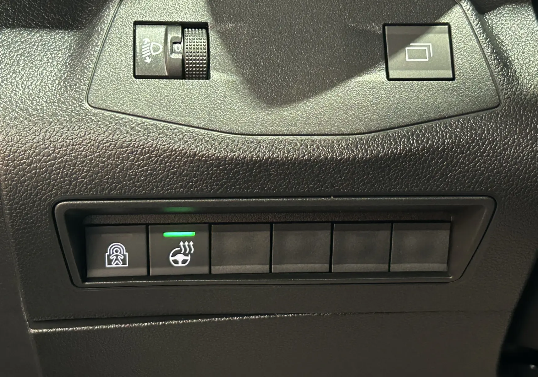 Gros plan sur les commandes noires du tableau de bord du Citroën Berlingo Multispace gris, avec bouton de chauffage de volant allumé.