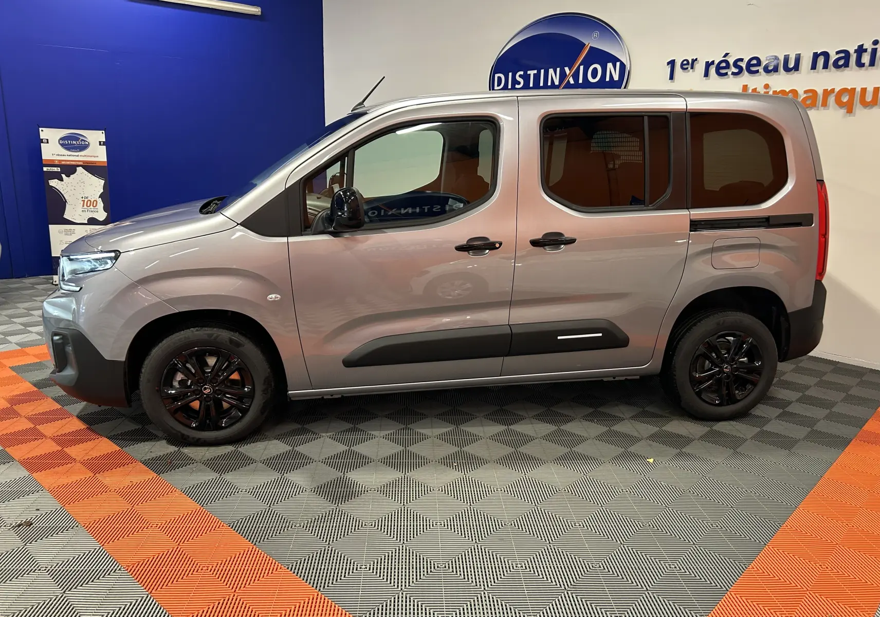 Profil côté gauche du Citroën Berlingo Multispace gris Artense avec jantes noires dans un showroom.