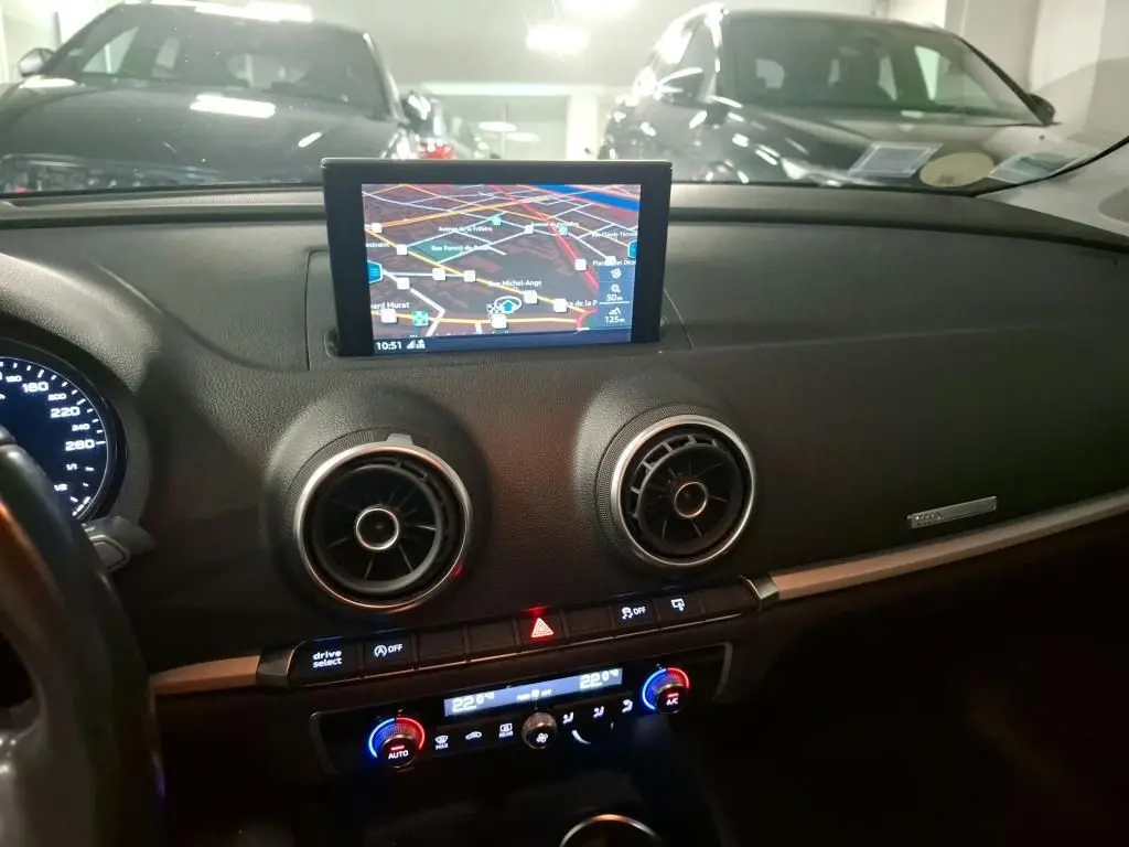 Vue intérieure du tableau de bord noir d'Audi A3 Sportback 2017 avec écran GPS central et aérateurs ronds chromés.