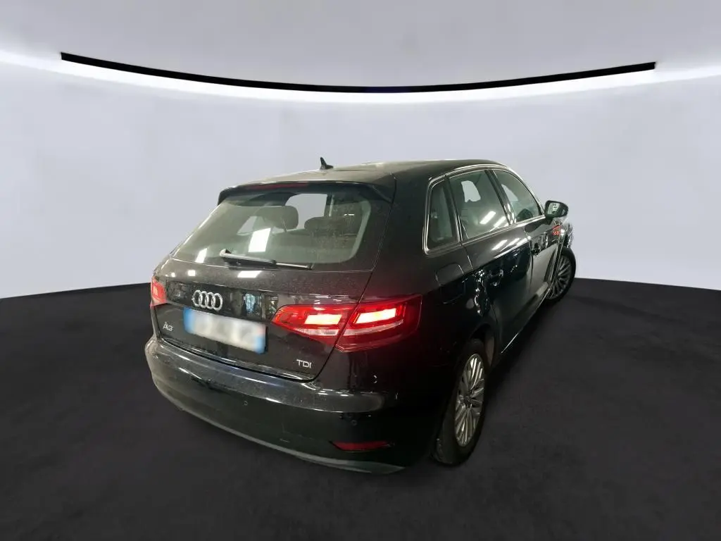 Audi A3 Sportback noire vue 3/4 arrière droit, feux arrière allumés dans un studio lumineux.