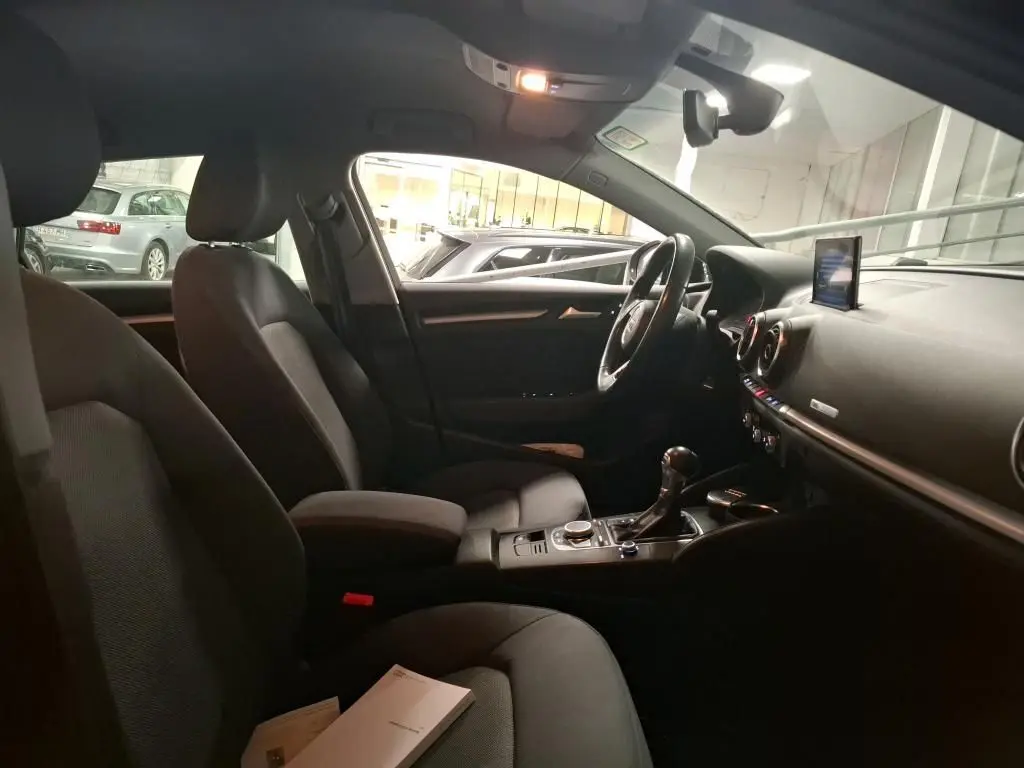 Vue intérieure côté conducteur de l'Audi A3 Sportback noire, montrant sièges, volant cuir et tableau de bord avec écran central.