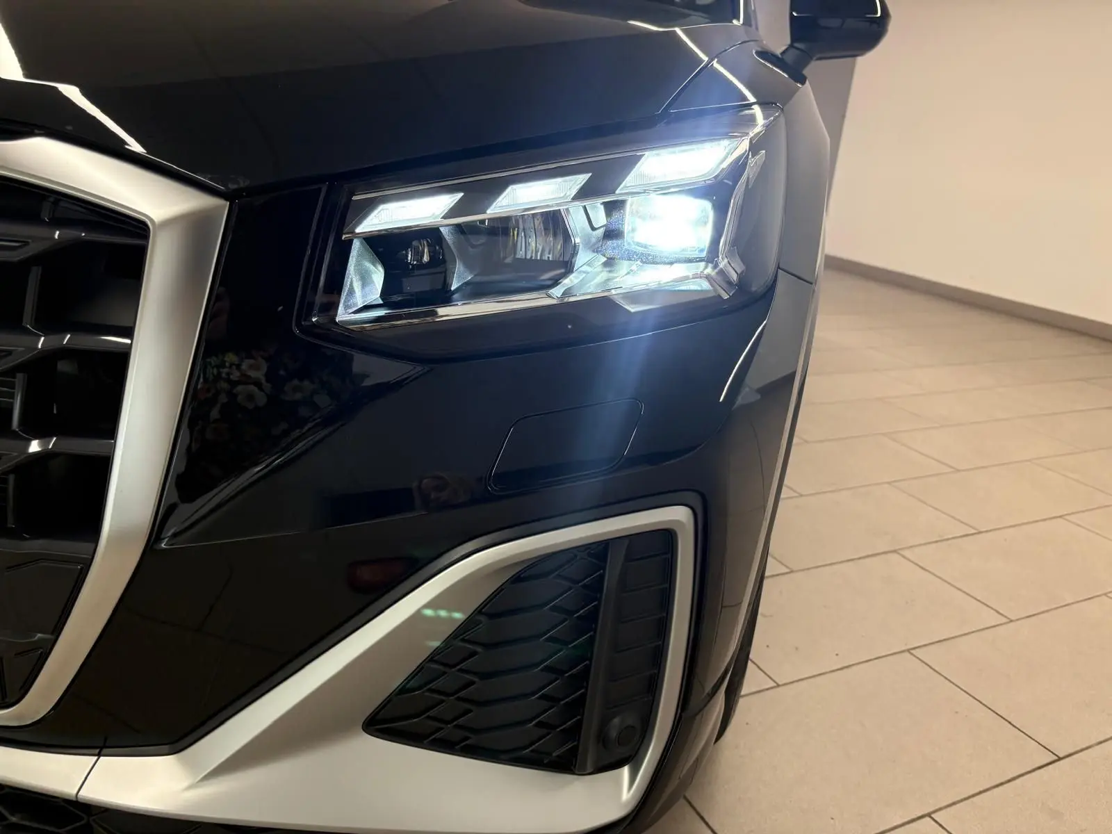 Gros plan sur le phare avant droit allumé d’un Audi Q2 35 TFSI S Line noir mythic, avec calandre et partie basse argentées.