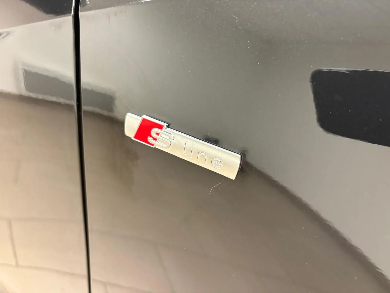 Gros plan sur l'emblème S line argent et rouge sur la porte noire métallisée d'un Audi Q2 35 TFSI 2026.