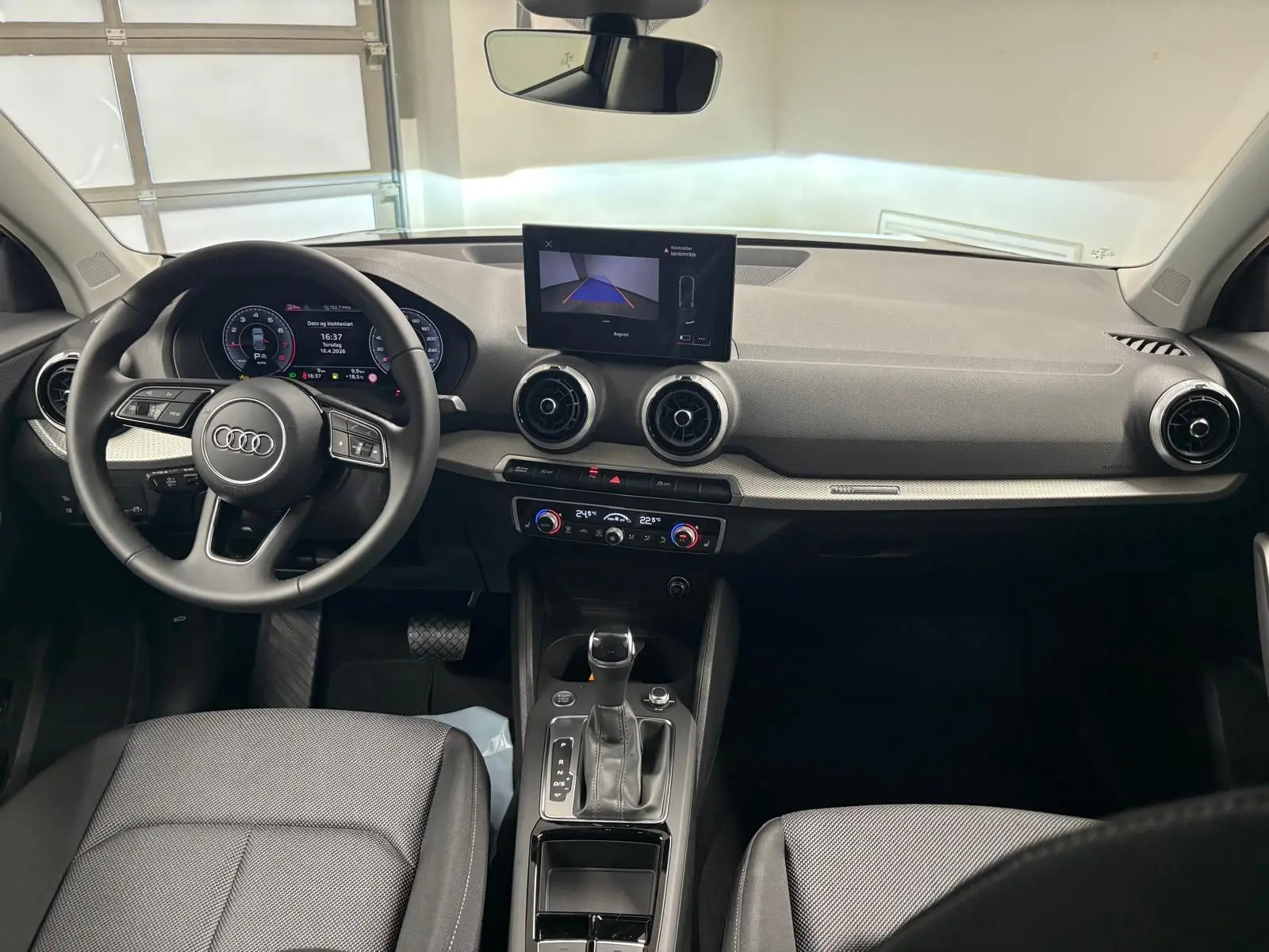 Vue intérieure avant de l'Audi Q2 35 TFSI S Line 2026, tableau de bord noir avec écran central et volant multifonction.