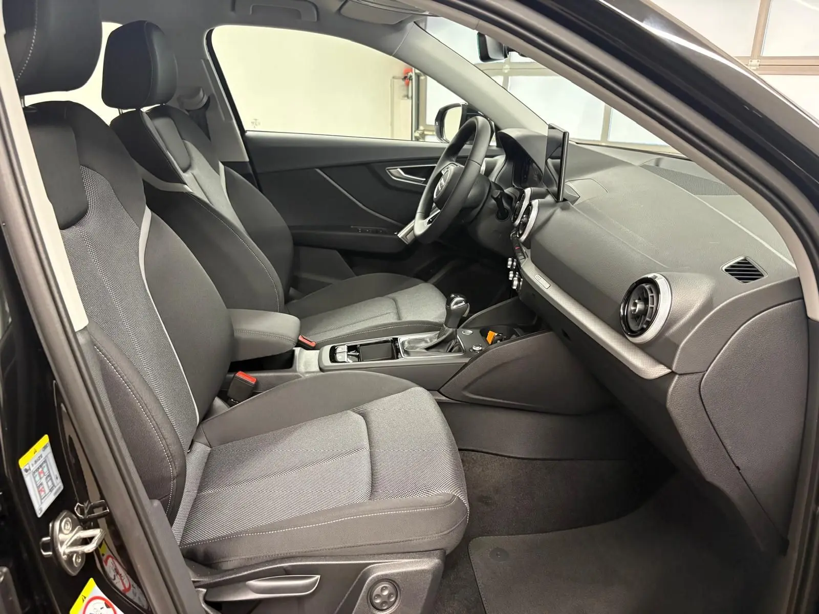 Vue intérieure côté gauche de l'Audi Q2 35 TFSI S Line 2026 en Noir Mythic, montrant sièges avant et tableau de bord.