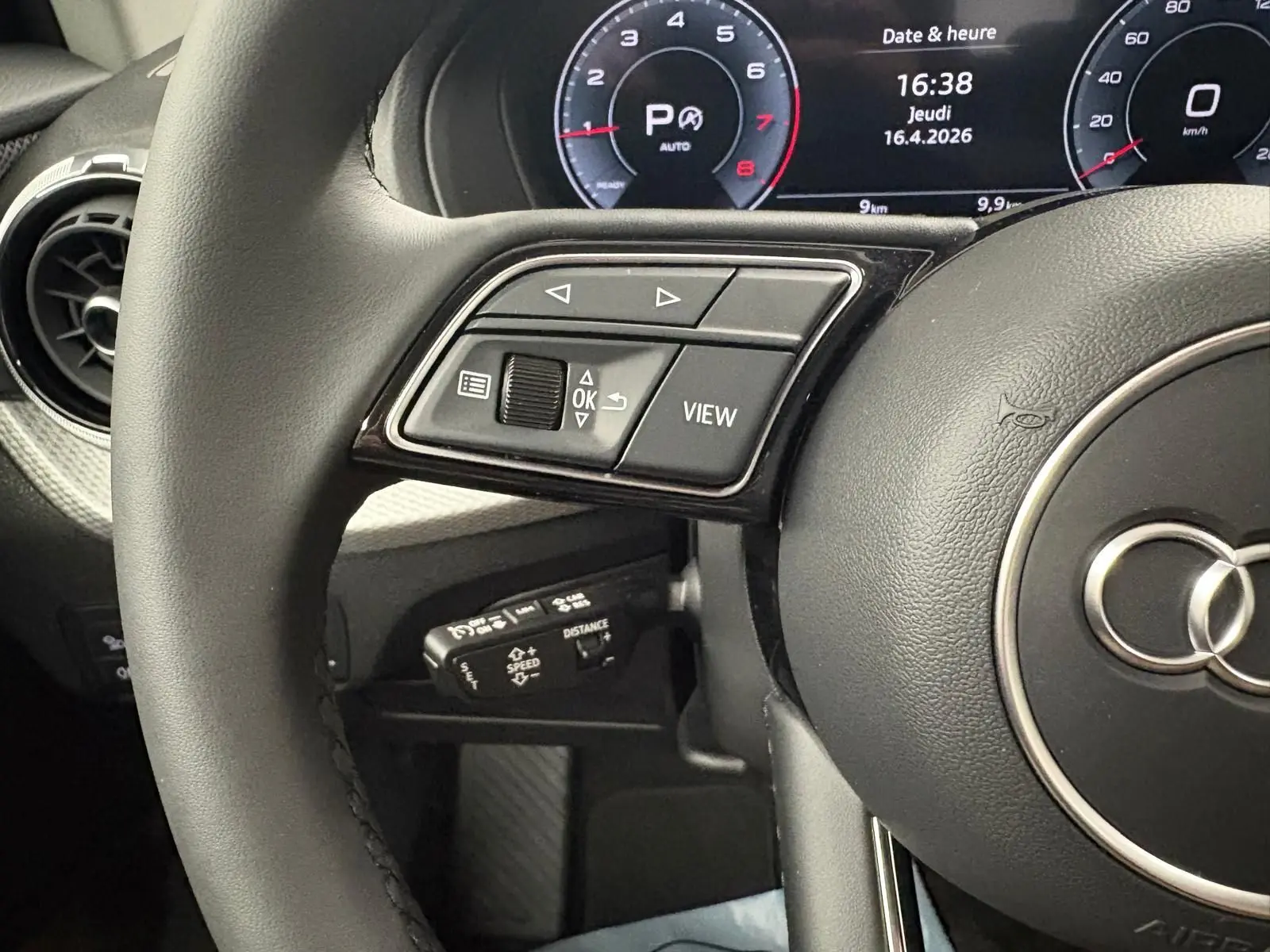 Gros plan sur le volant noir et le tableau de bord numérique de l'Audi Q2 35 TFSI S Line 2026, affichant l'heure et la vitesse.
