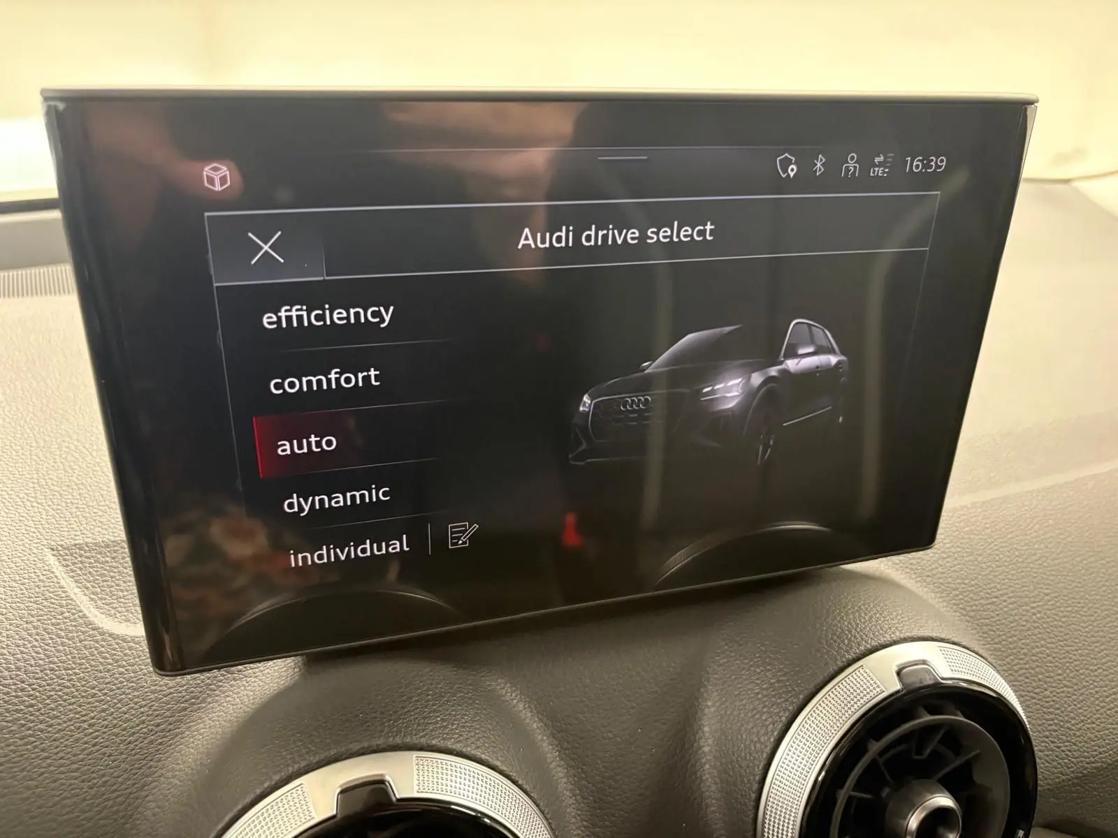 Écran central affichant le menu Audi drive select avec une illustration du SUV Audi Q2 noir Mythic en vue de face.