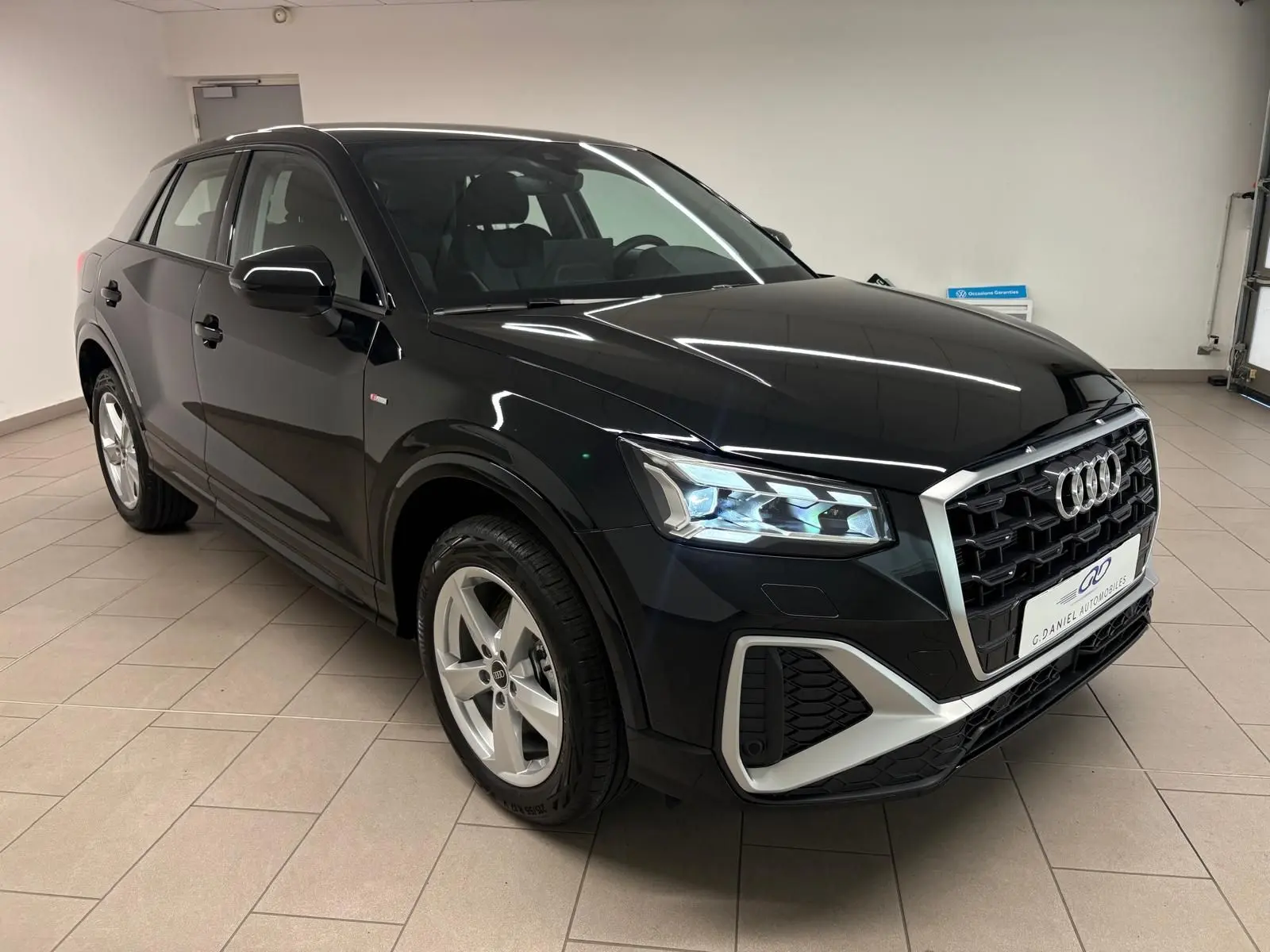 Audi Q2 35 TFSI S line noir mythic en 3/4 avant droit, mettant en valeur ses phares LED et sa calandre distinctive.