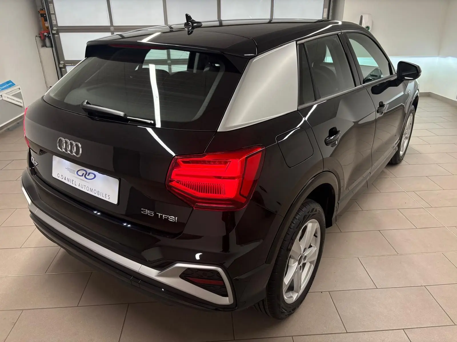 Audi Q2 35 TFSI noir mythic vue 3/4 arrière droit, avec toit contrastant gris et feux arrière allumés.