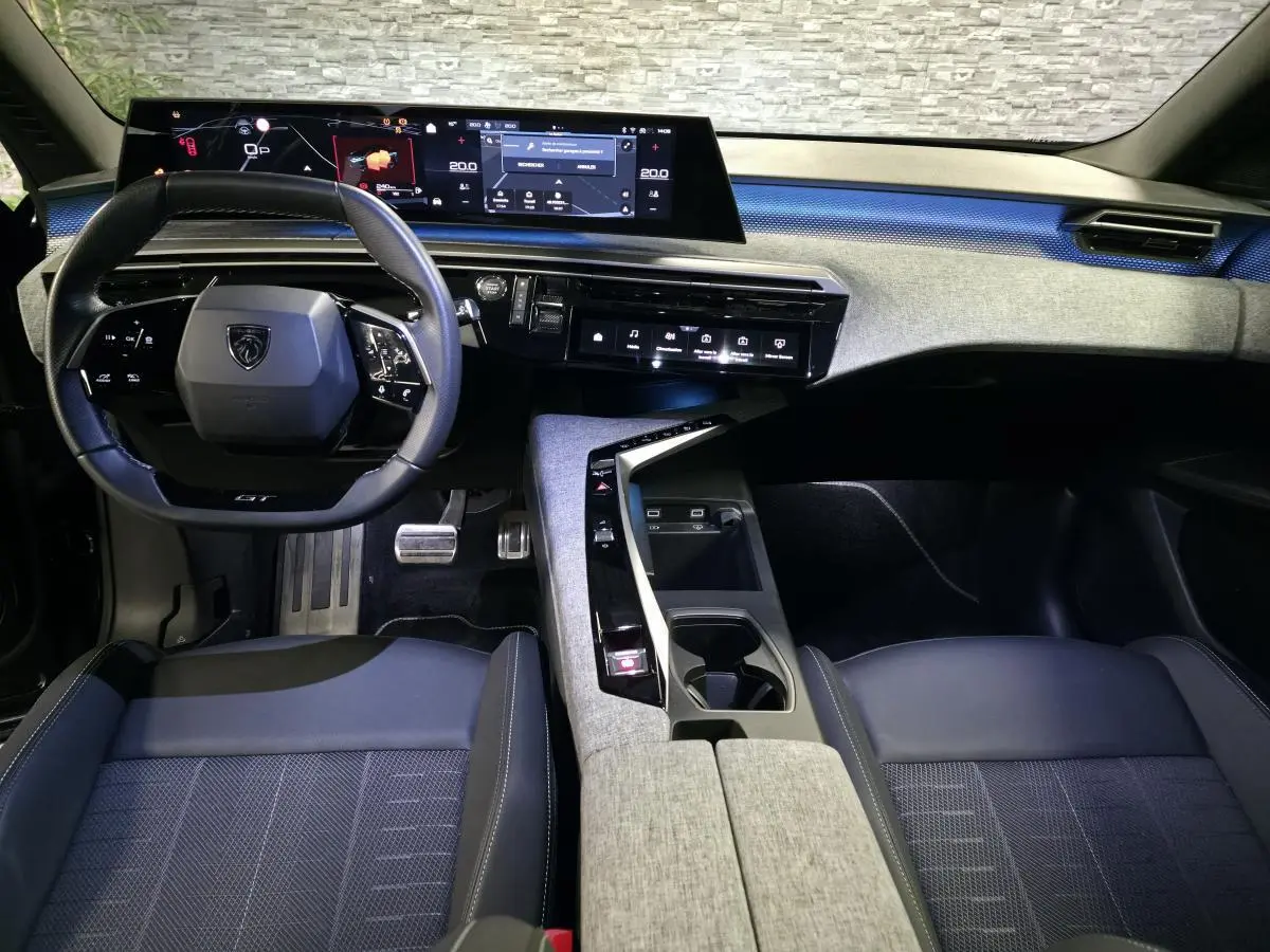 Vue intérieure avant du Peugeot 3008 2025 noir, tableau de bord avec écran panoramique et volant compact GT.
