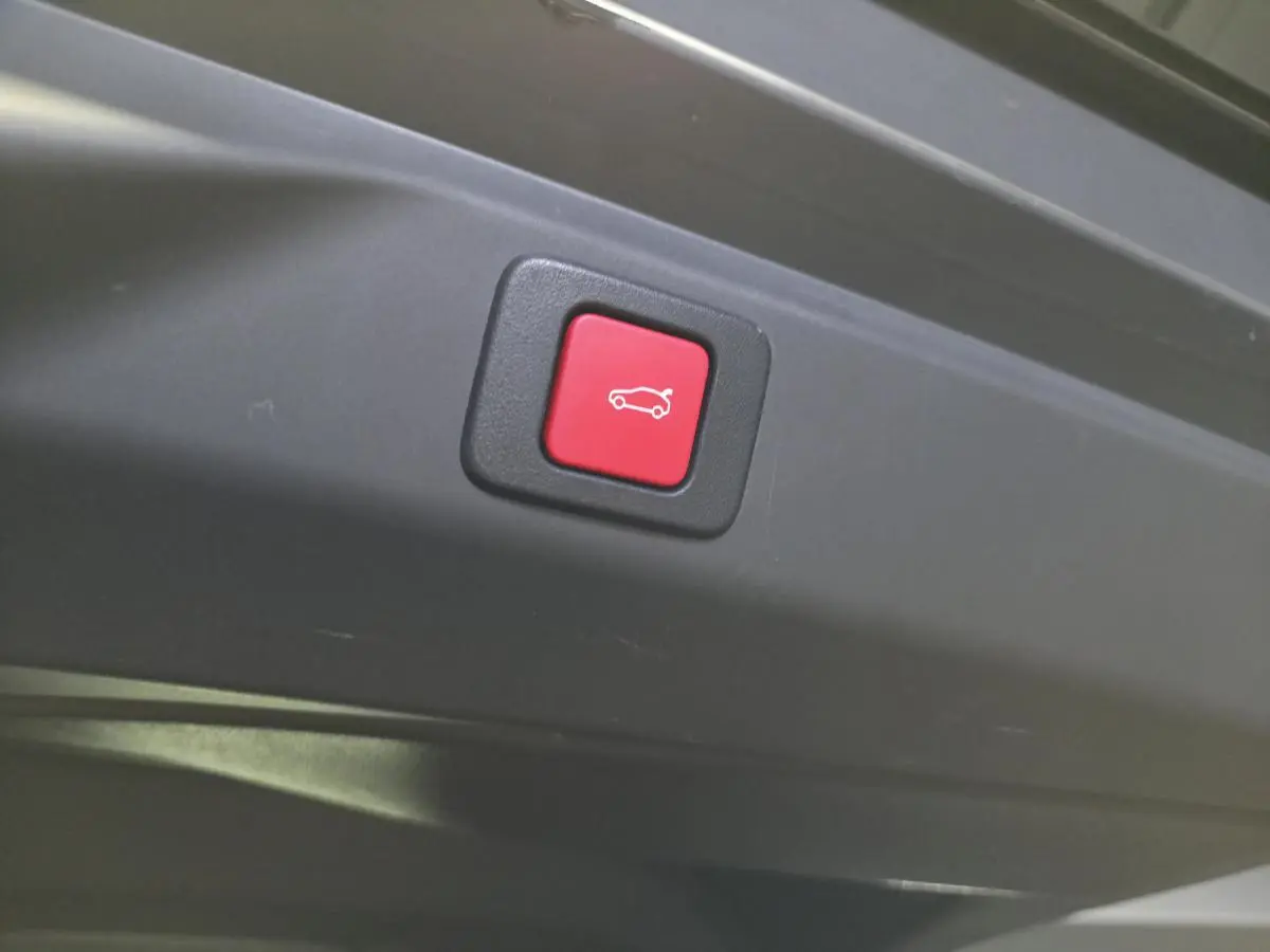 Bouton rouge d'ouverture électrique du hayon sur le bord intérieur d'un Peugeot 3008 noir hybride 2025.