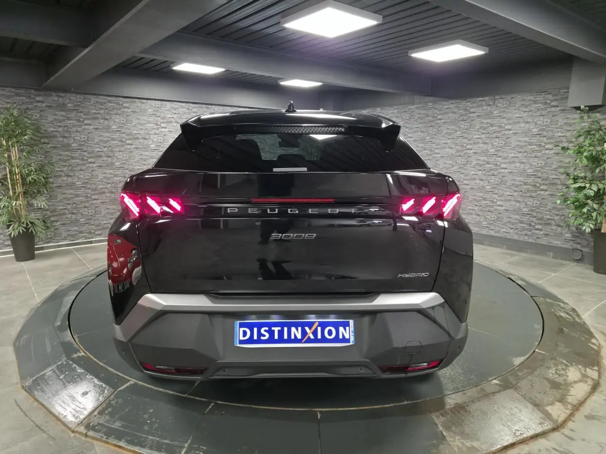 Vue arrière d'un Peugeot 3008 noir hybride 2025 avec feux arrière à griffes LED allumés dans un showroom.
