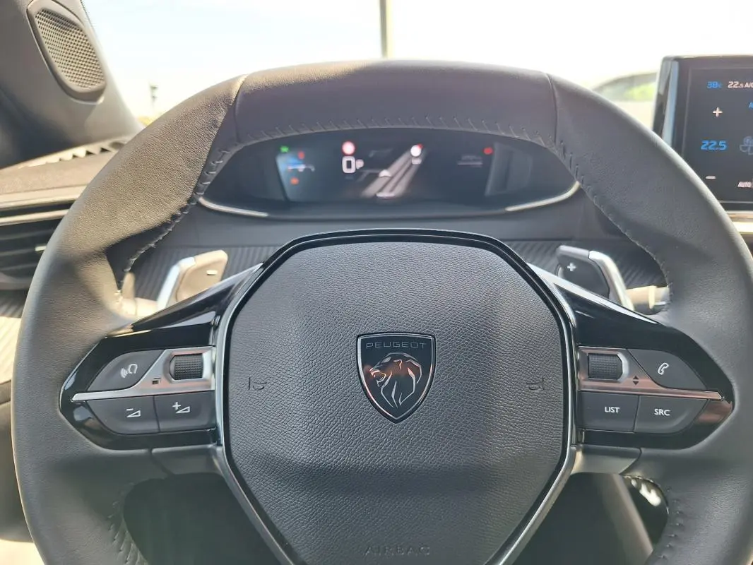 Vue rapprochée du volant noir de la Peugeot 2008 Hybrid 136 e-DCS6 Allure avec commandes intégrées et tableau de bord numérique.