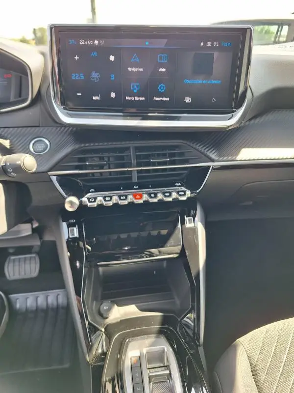 Vue intérieure centrée sur la console centrale et l'écran tactile du Peugeot 2008 Hybrid noir avec commandes piano et finition brillante.