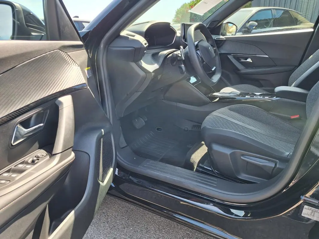 Vue intérieure côté conducteur de la Peugeot 2008 Hybrid noire, mettant en valeur le tableau de bord et les sièges tissu.