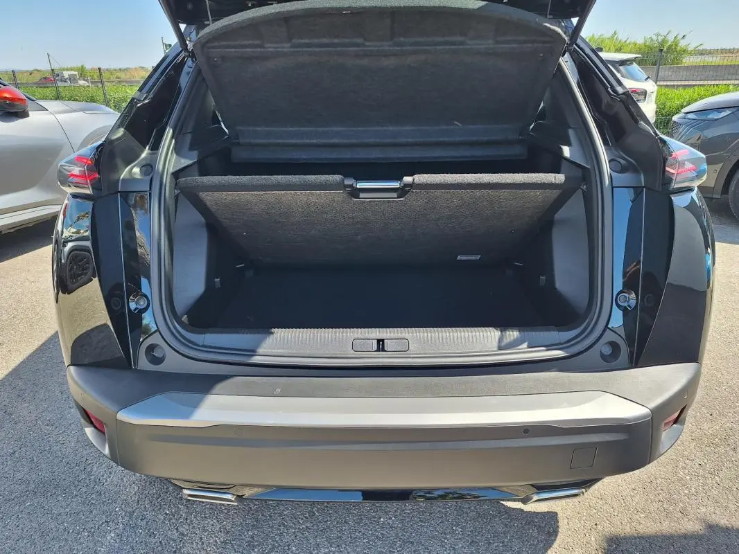 Vue arrière du coffre ouvert d’un Peugeot 2008 Hybrid 136 noir, avec barres de toit visibles sur le dessus.