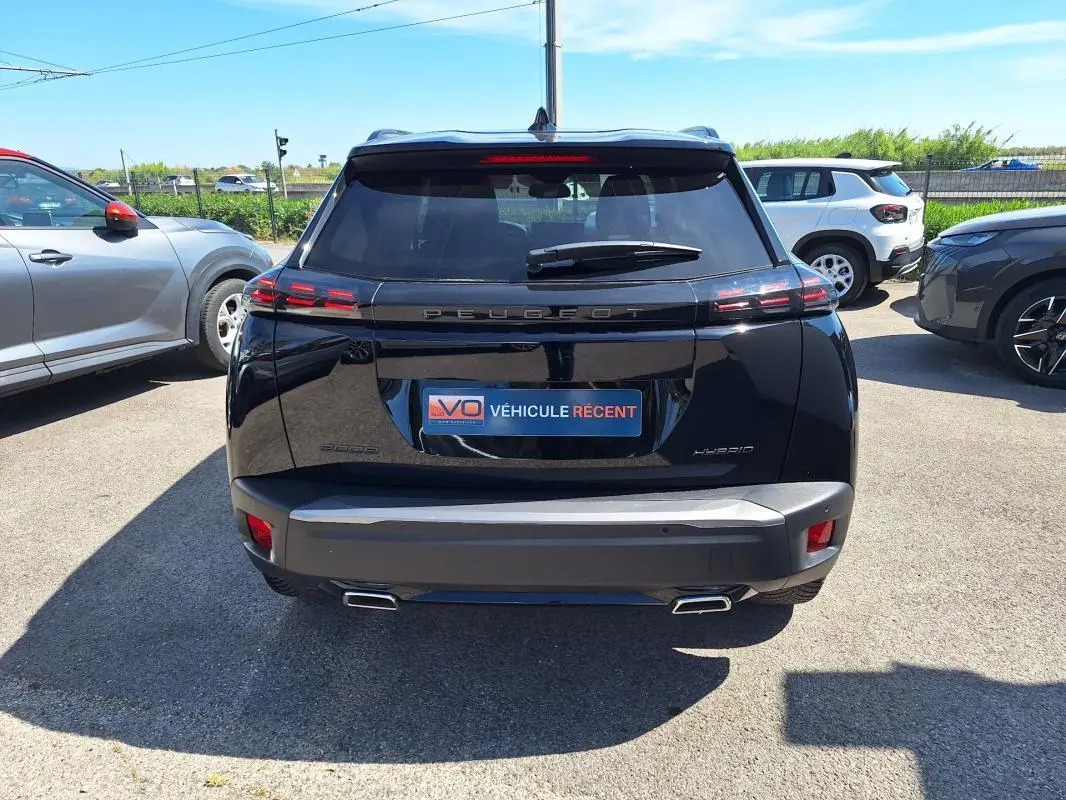 Vue arrière d’un Peugeot 2008 Hybrid noir 2025 avec barres de toit et jantes alliage 17 pouces, en extérieur.