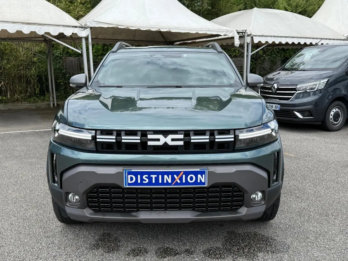 Vue avant d'un Dacia Duster Hybrid 140 Journey vert cèdre avec calandre noire et phares LED allumés.