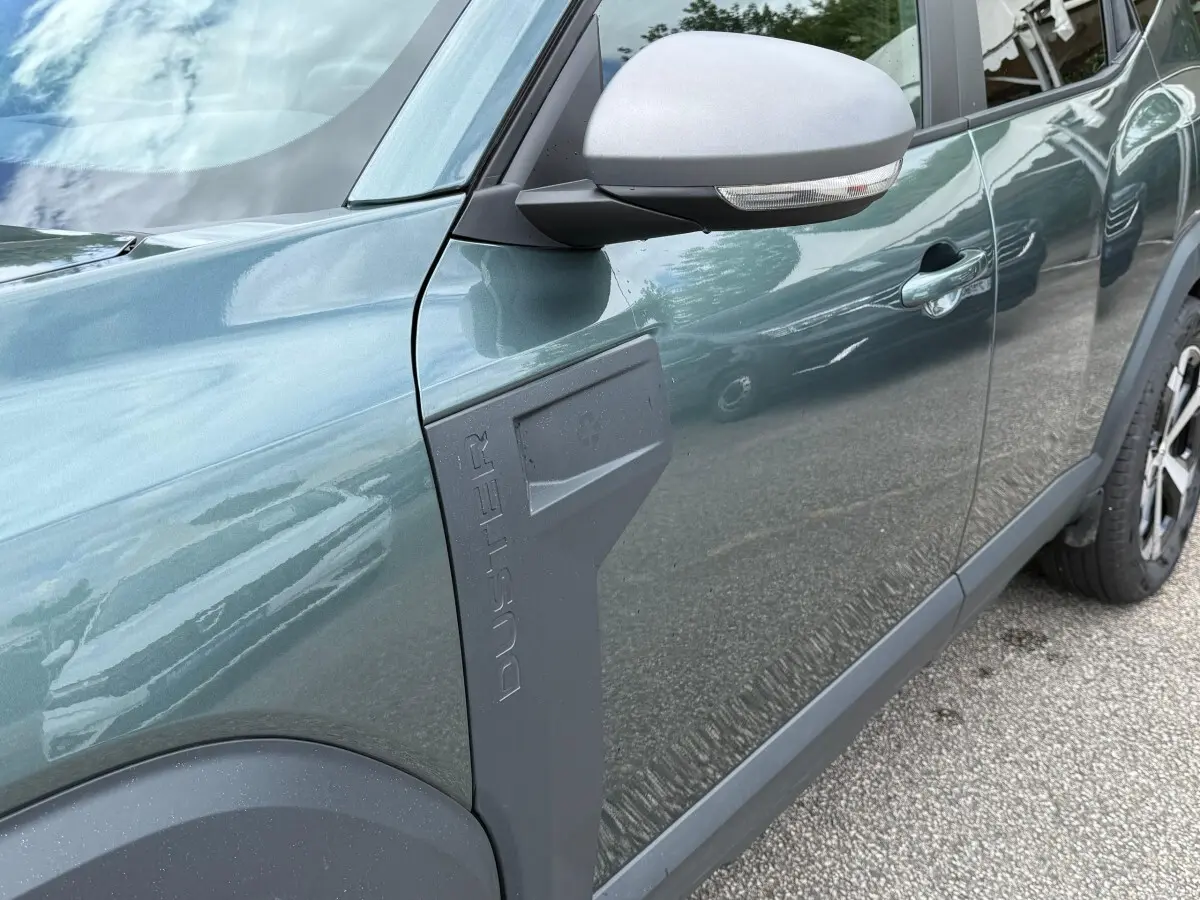 Vue latérale côté gauche du Dacia Duster Hybrid 140 Journey vert cèdre avec logo Duster en relief sur l'aile avant.