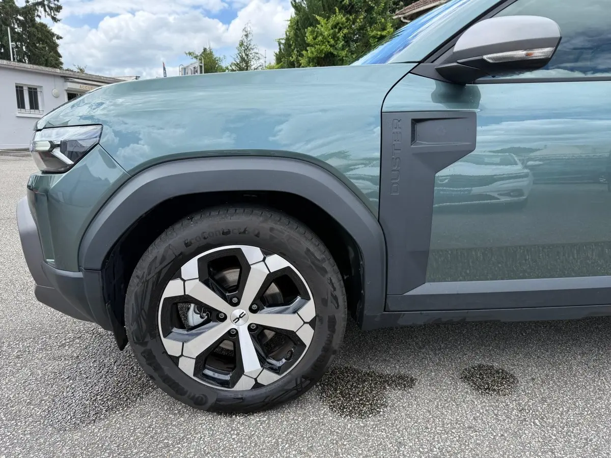Vue de profil côté avant gauche du Dacia Duster Hybrid 140 Journey vert cèdre avec jante alliage et logo Duster sur l'aile.