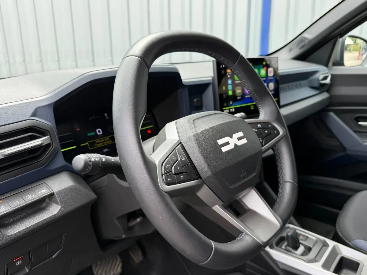 Vue intérieure rapprochée du volant multifonctions en cuir synthétique du Dacia Duster Hybrid 140 Journey 2025.