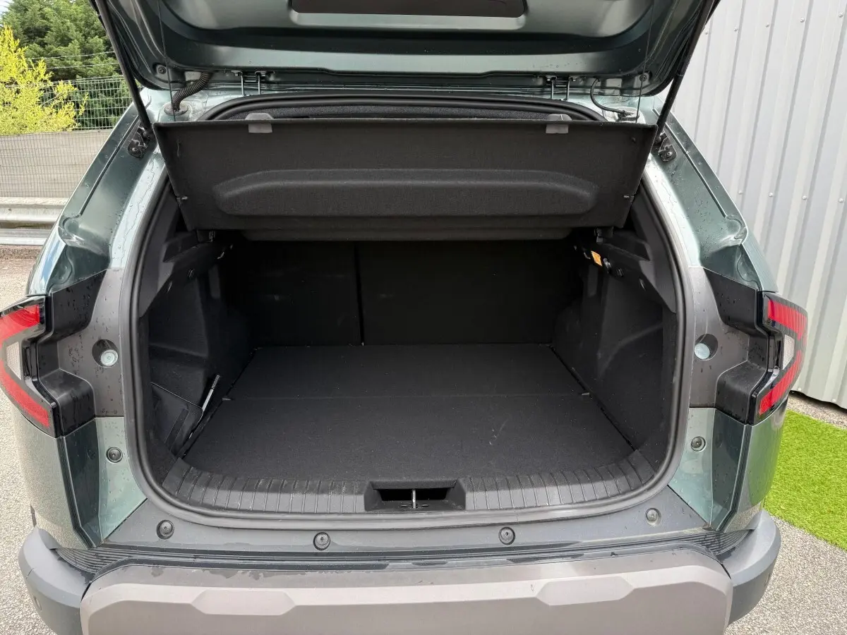 Coffre ouvert vu de l'arrière du Dacia Duster Hybrid 140 Journey vert cèdre, montrant un espace de chargement vide.