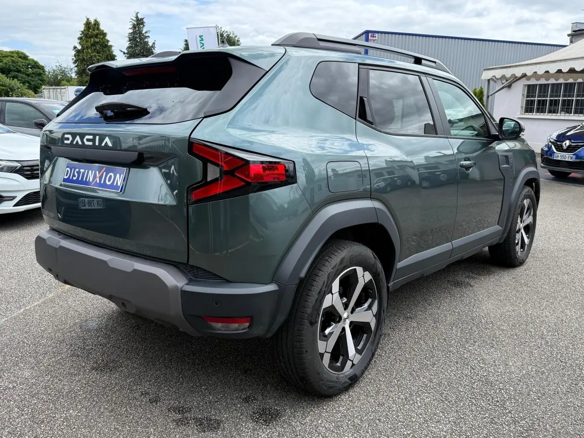 Vue 3/4 arrière droite du Dacia Duster Hybrid 140 Journey vert cèdre avec jantes alliage et barres de toit noires.
