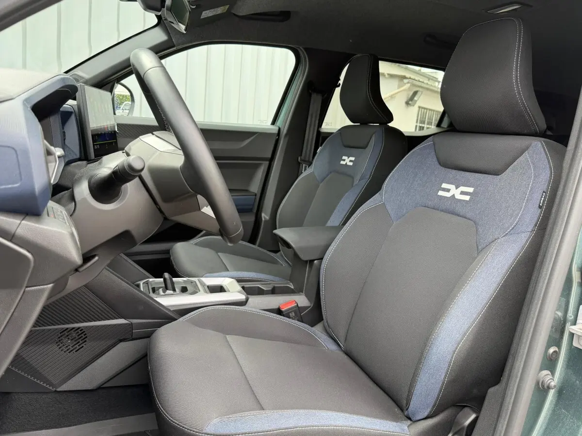 Vue intérieure côté conducteur du Dacia Duster Hybrid 140 Journey avec sièges bi-matière noirs et bleus et volant multifonctions.