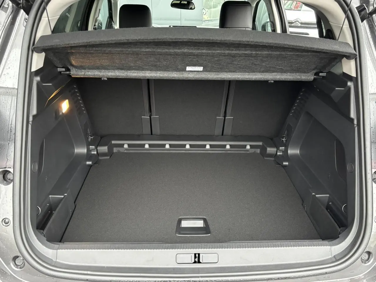 Coffre ouvert vu de l'arrière d'un Citroën C5 Aircross gris Platinium, avec cache-bagages relevé et intérieur noir.