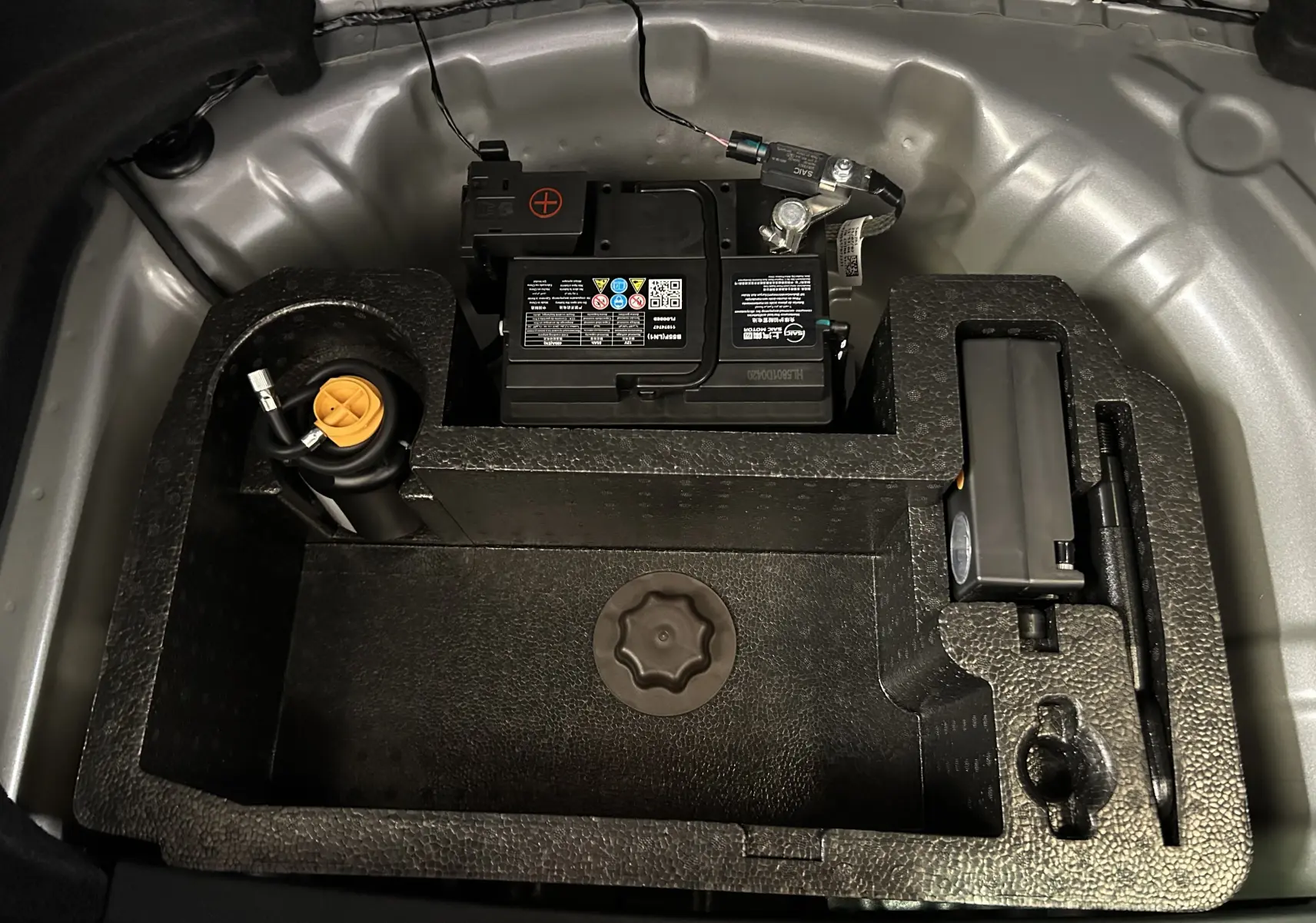 Vue rapprochée du compartiment de rangement sous le coffre du MG3 1.5 Hybrid+ 195 Luxury, avec batterie et accessoires.