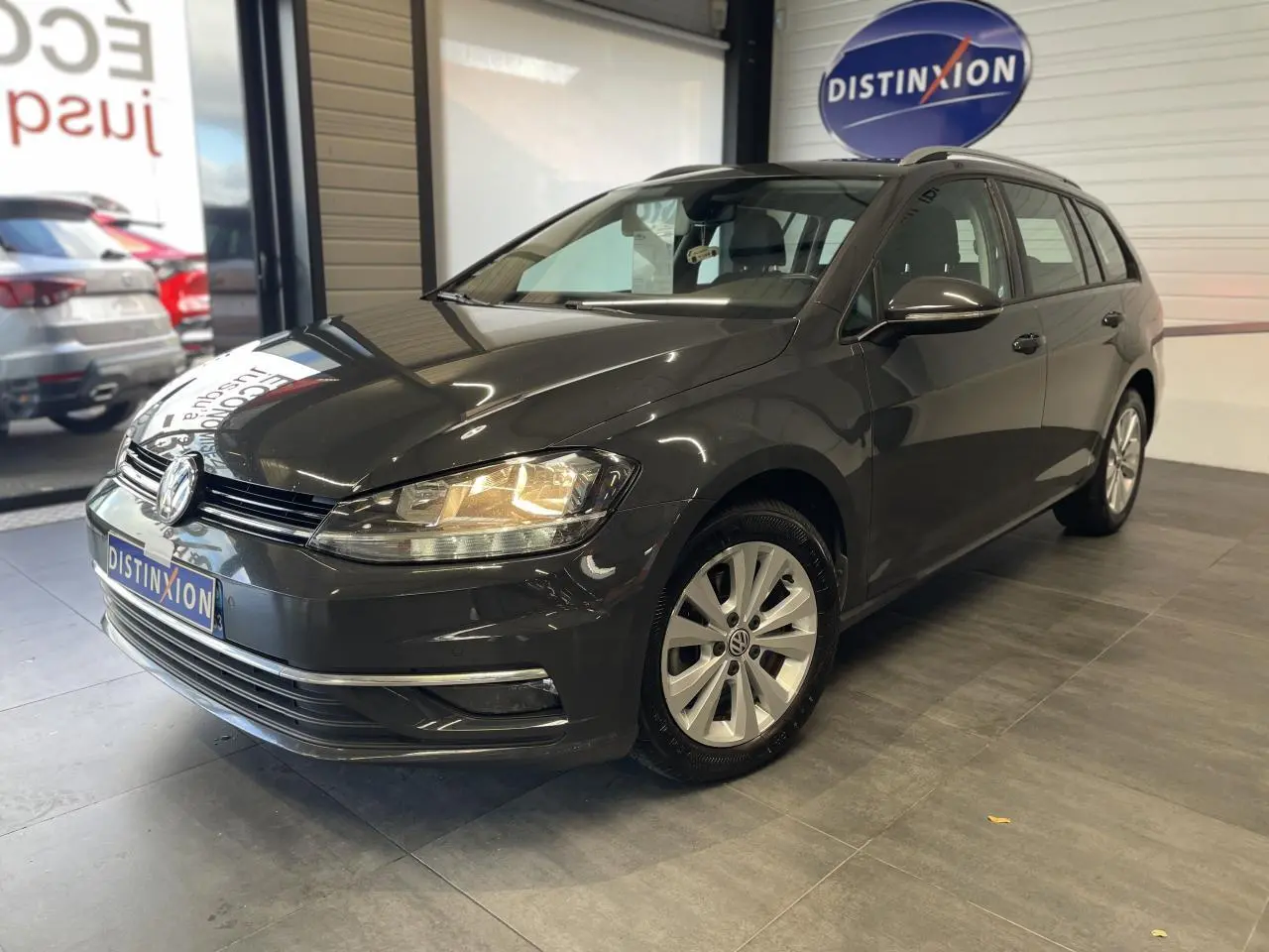 Volkswagen Golf SW gris foncé vue 3/4 avant droit en intérieur avec phares allumés et jantes alliage 16 pouces.