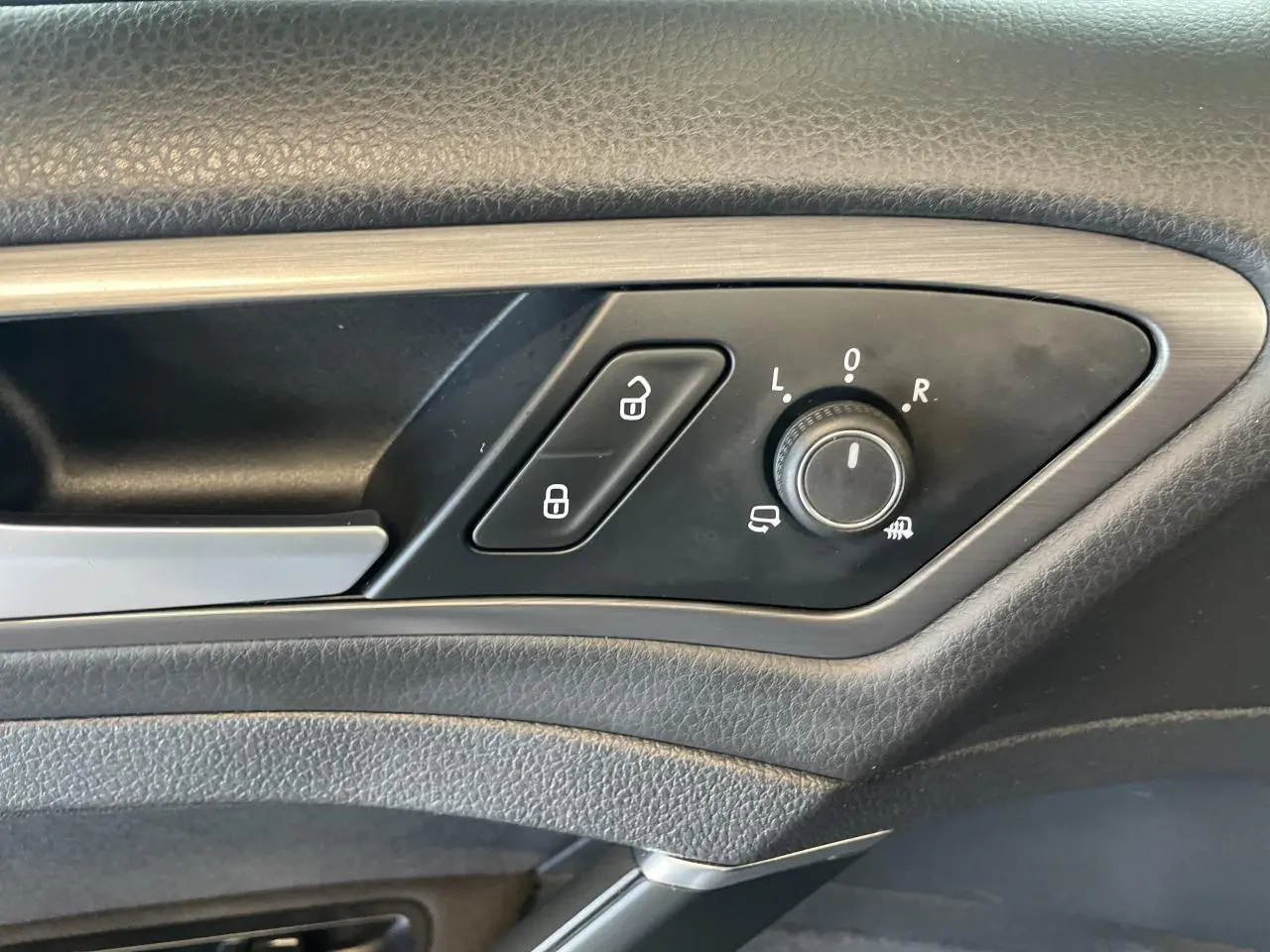Détail de la commande de réglage des rétroviseurs et verrouillage sur la porte côté conducteur d'une Volkswagen Golf SW gris foncé.