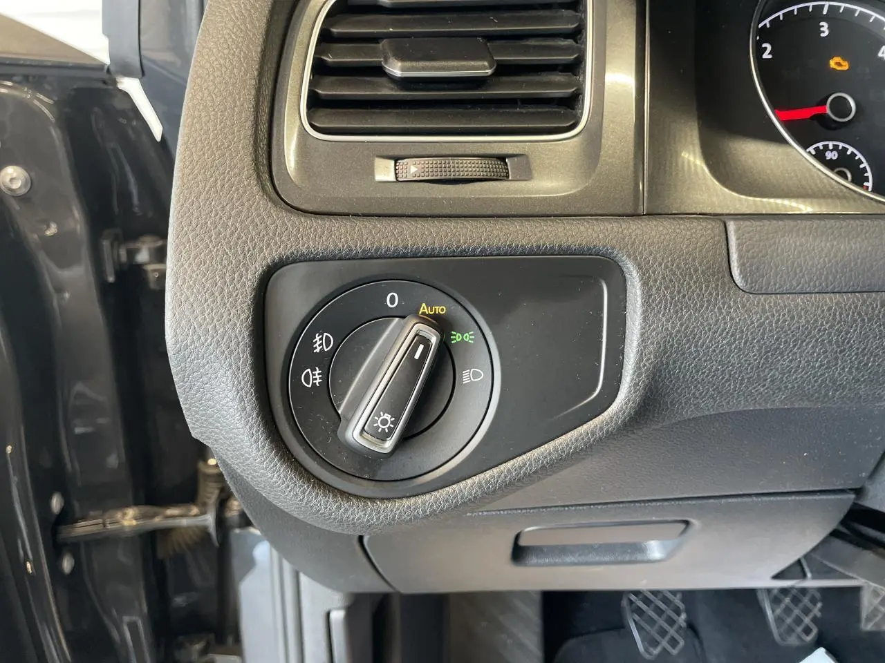 Vue rapprochée du tableau de bord côté gauche d'une Volkswagen Golf gris foncé, avec commande des phares en mode auto.