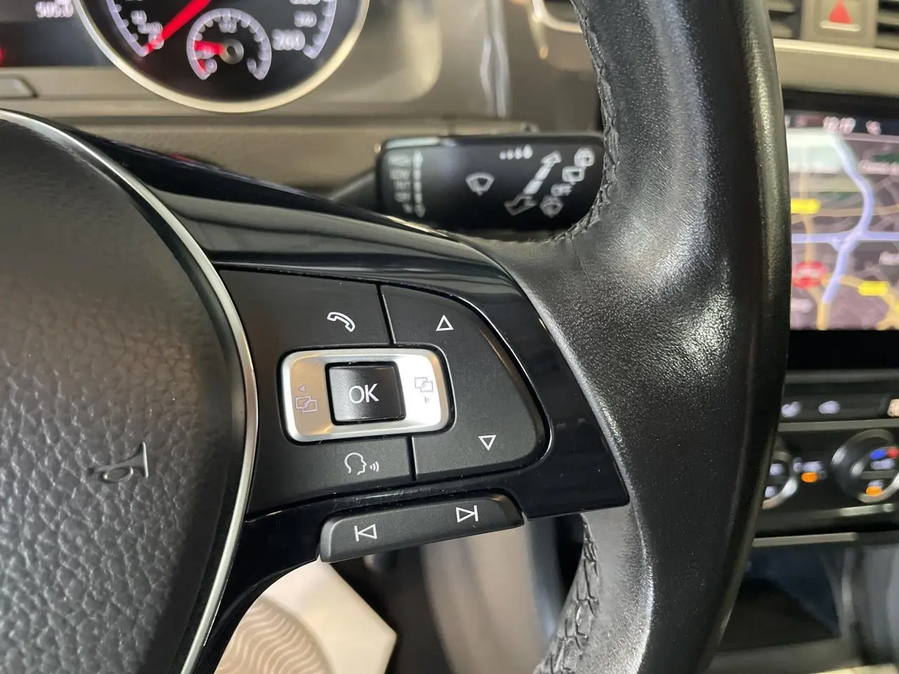 Gros plan sur les commandes gauche du volant cuir noir d'une Volkswagen Golf SW 1.6 TDI 2017 avec tableau de bord et écran tactile en arrière-plan.