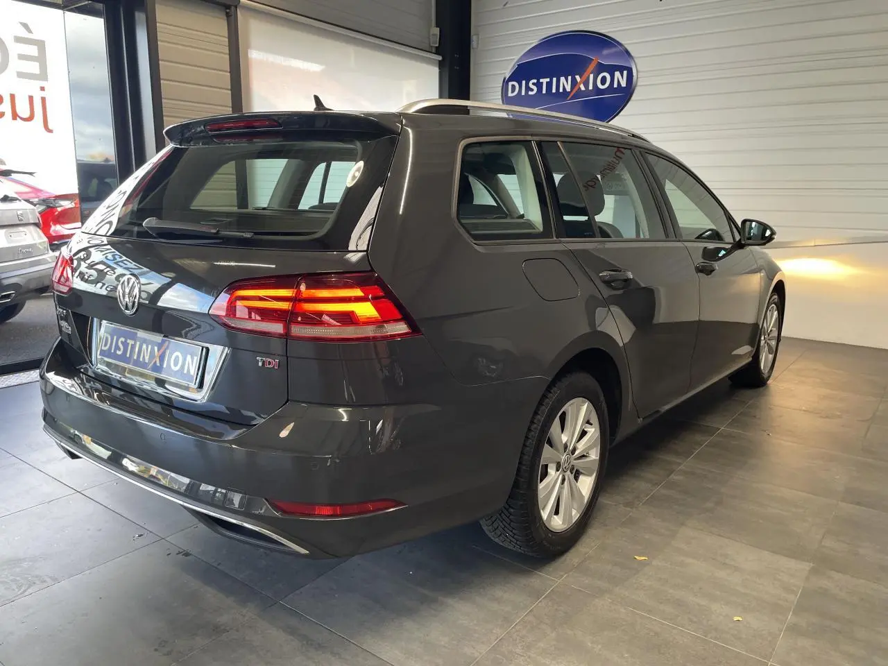 Volkswagen Golf SW gris foncé vue 3/4 arrière droit avec feux arrière allumés en intérieur showroom.
