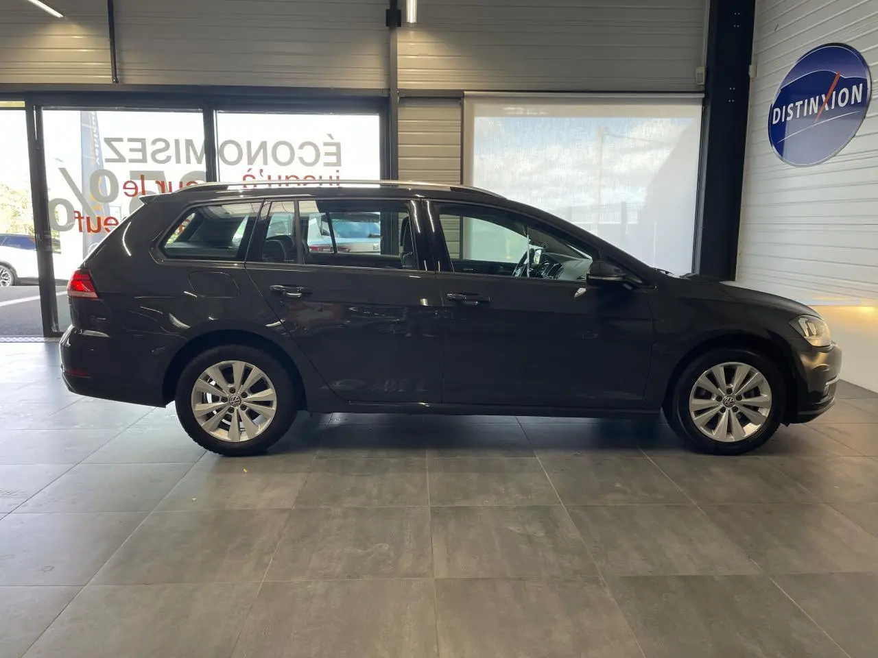 Profil côté gauche d'une Volkswagen Golf SW gris foncé 2017 avec jantes alliage et vitres teintées en intérieur showroom.