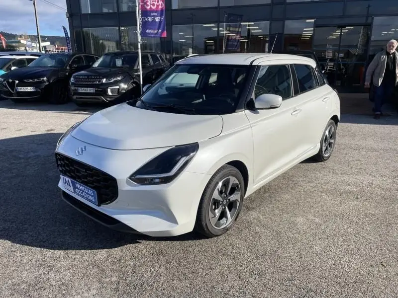 Suzuki Swift 1.2 Hybrid blanc vue 3/4 avant droit, avec jantes alliage et calandre noire distinctive.