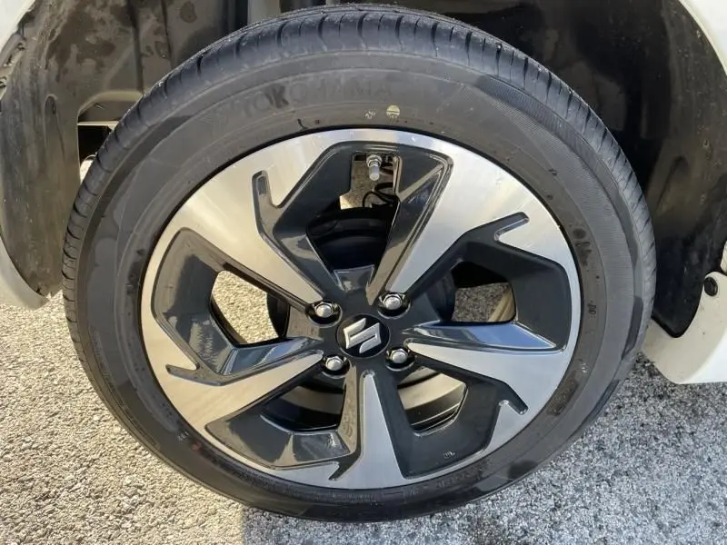 Gros plan sur la roue avant droite d'une Suzuki Swift blanche 2025, jante alliage bicolore avec logo Suzuki central.