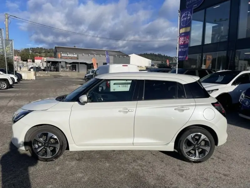 Vue de profil côté gauche d'une Suzuki Swift blanche 2025 avec toit noir et jantes alliage foncé, stationnée en extérieur.