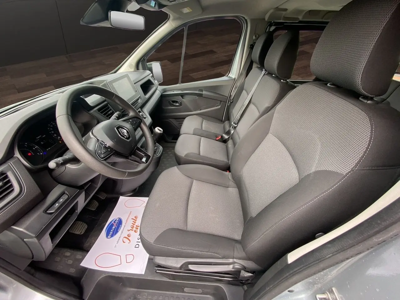Vue intérieure côté conducteur du Renault Trafic Combi gris platine 2023, montrant les sièges tissu noirs et le tableau de bord moderne.
