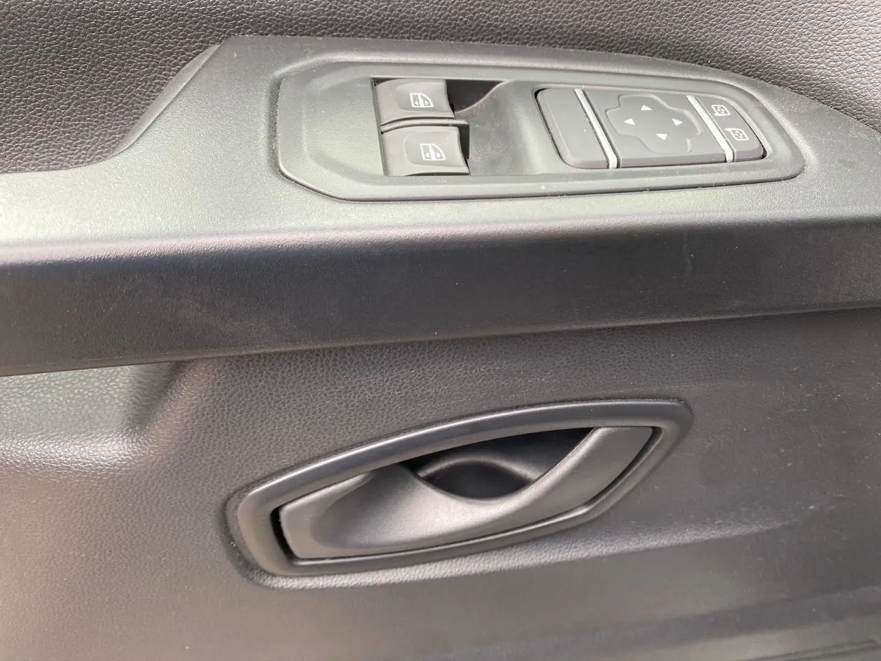 Gros plan sur la poignée intérieure et les commandes de lève-vitres côté conducteur du Renault Trafic Combi gris platine 2023.