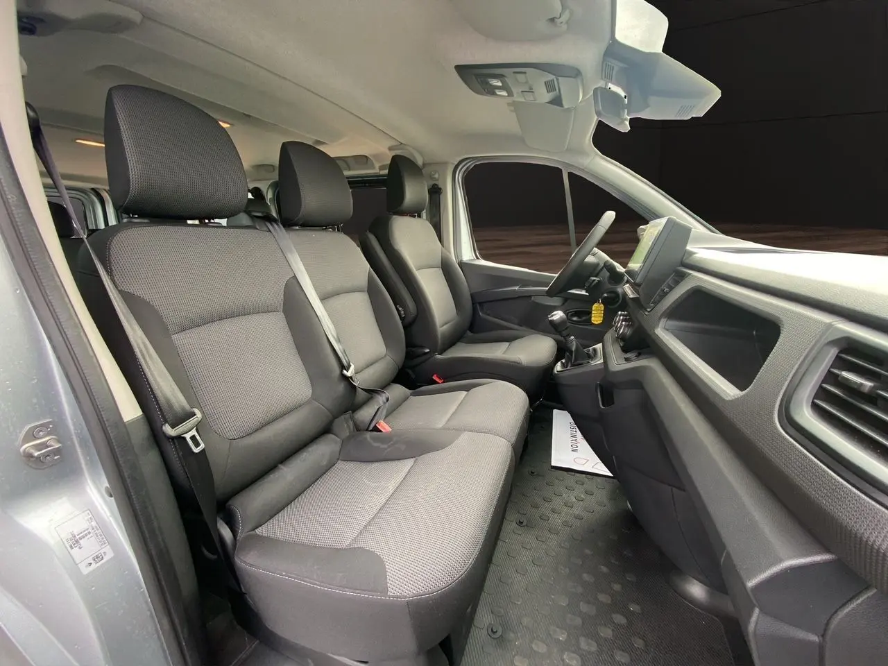 Vue intérieure côté gauche du Renault Trafic Combi 2023 gris platine, montrant les sièges avant en tissu noir et tableau de bord.