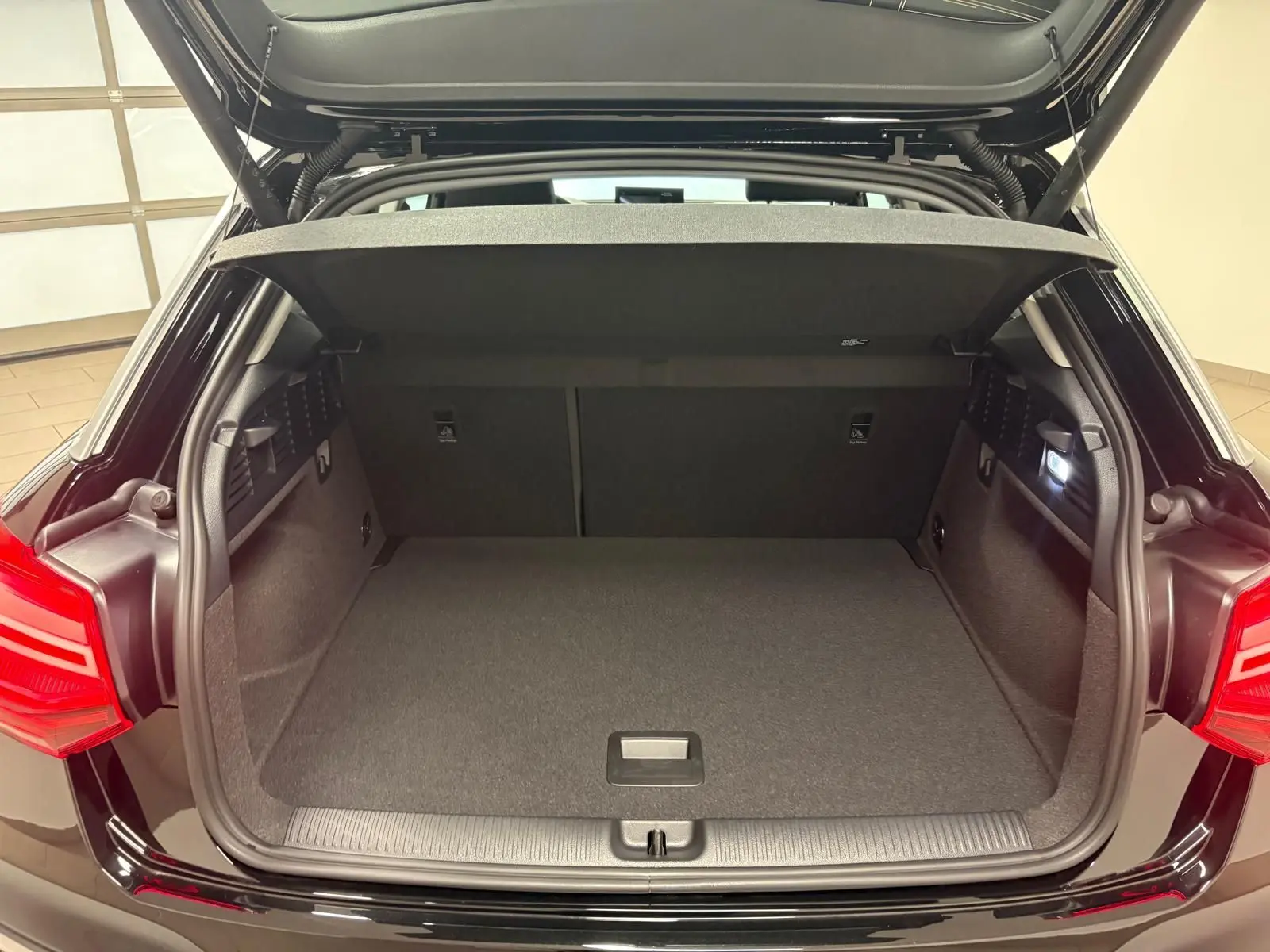 Coffre ouvert vu de l'arrière d'un Audi Q2 Noir Mythic, montrant l'espace de chargement et le hayon électrique.