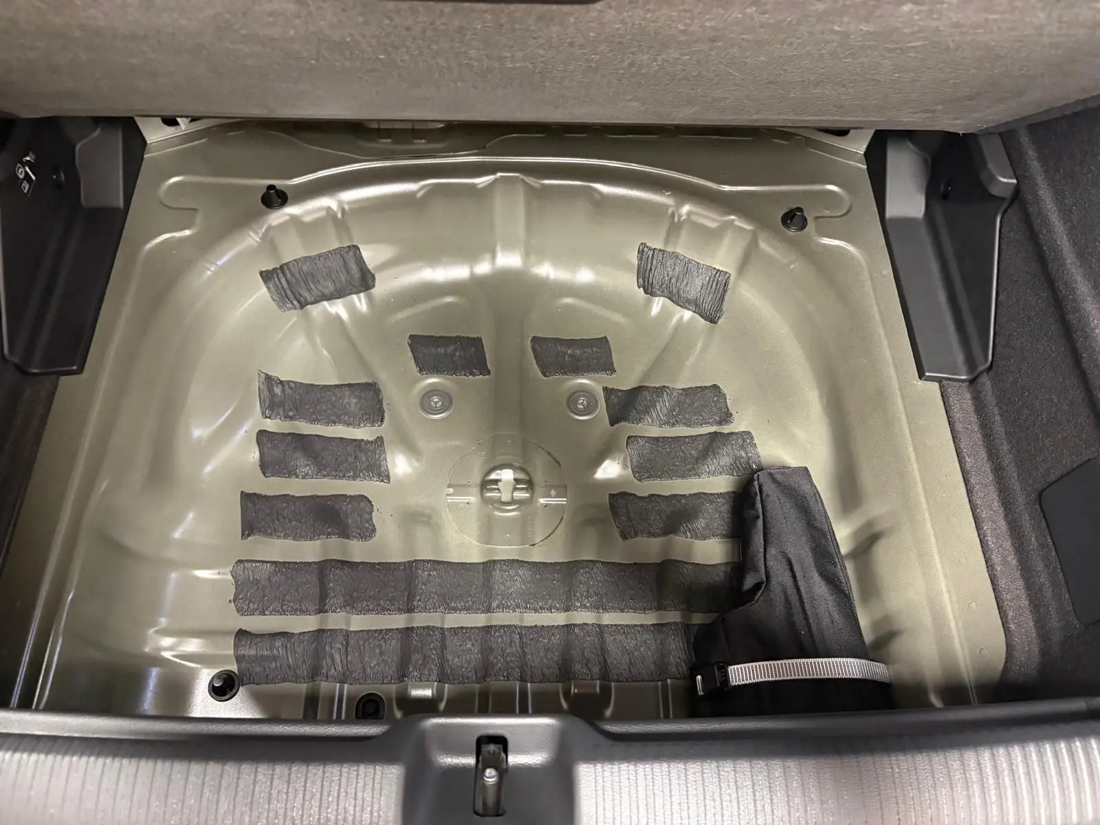 Coffre ouvert d’un Audi Q2 35 TFSI S Line 2026 montrant le logement métallique de la roue de secours sans pneu.