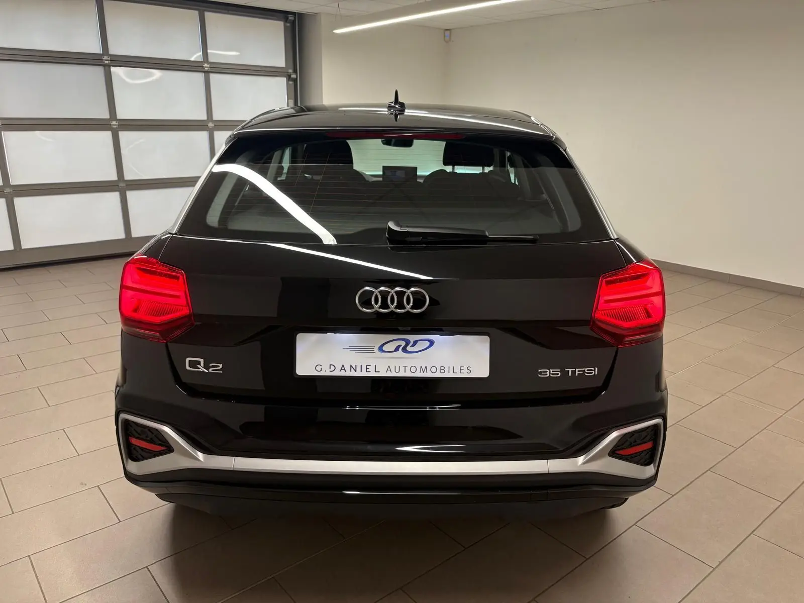 Vue arrière d'un Audi Q2 35 TFSI noir mythic avec feux rouges allumés dans un garage intérieur.