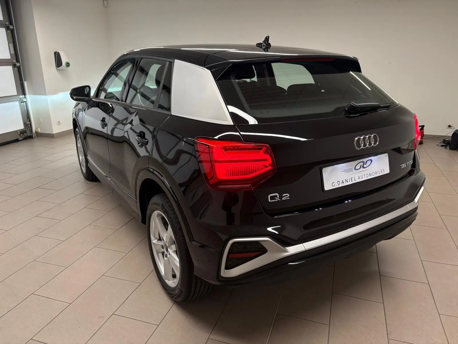 Audi Q2 35 TFSI S Line noir mythic vu en 3/4 arrière droit, avec toit et montant arrière contrastés argentés.